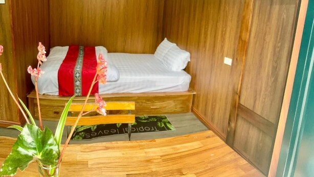 A compact room with a bed, wooden walls, a small table, and a window. - Cat Ba Love House (Hai Phong)