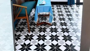 A room with a black and white patterned floor, a table with a blue tablecloth, a wooden chair, and a television mounted on the wall. - Cat Ba Love House (Hai Phong)