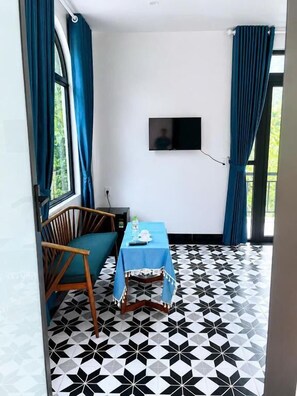 Una habitación con piso estampado en blanco y negro, una mesa con mantel azul, una silla de madera y un televisor montado en la pared.