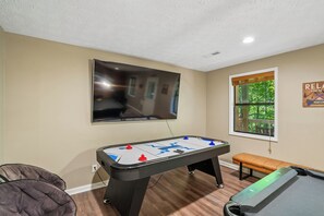Ein Zimmer mit einer Fußballstoßmaschine, einem an der Wand montierten Fernseher und einem Fenster mit Blick auf Grünflächen.