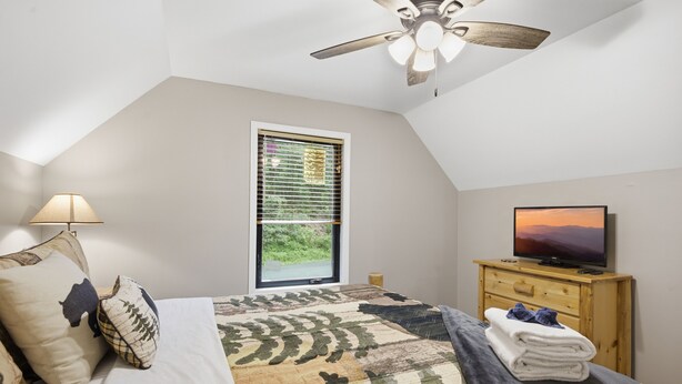 A bedroom with a bed, a ceiling fan, a television on a wooden dresser, and a window with blinds. - Bear Run Getaway | Near Downtown Gatlinburg (Gatlinburg)