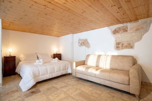 Ein Schlafzimmer mit einem Bett, einer Couch, einem Nachttisch und Steinböden.