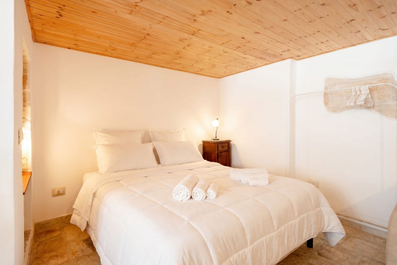 Une chambre avec un plafond en bois, un lit avec une literie blanche, une table de chevet et un porte-serviettes fixé au mur.