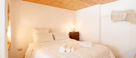 A bedroom with a wooden ceiling, a bed with white bedding, a nightstand, and a wall-mounted towel rack.