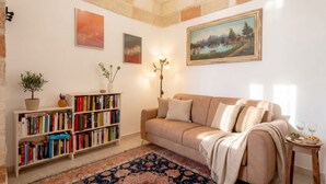 Ett mysigt vardagsrum med en beige soffa, en bokhylla, en tavla och en dekorativ lampa.