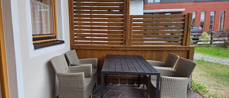 Um pátio externo com móveis de vime e uma mesa de madeira.