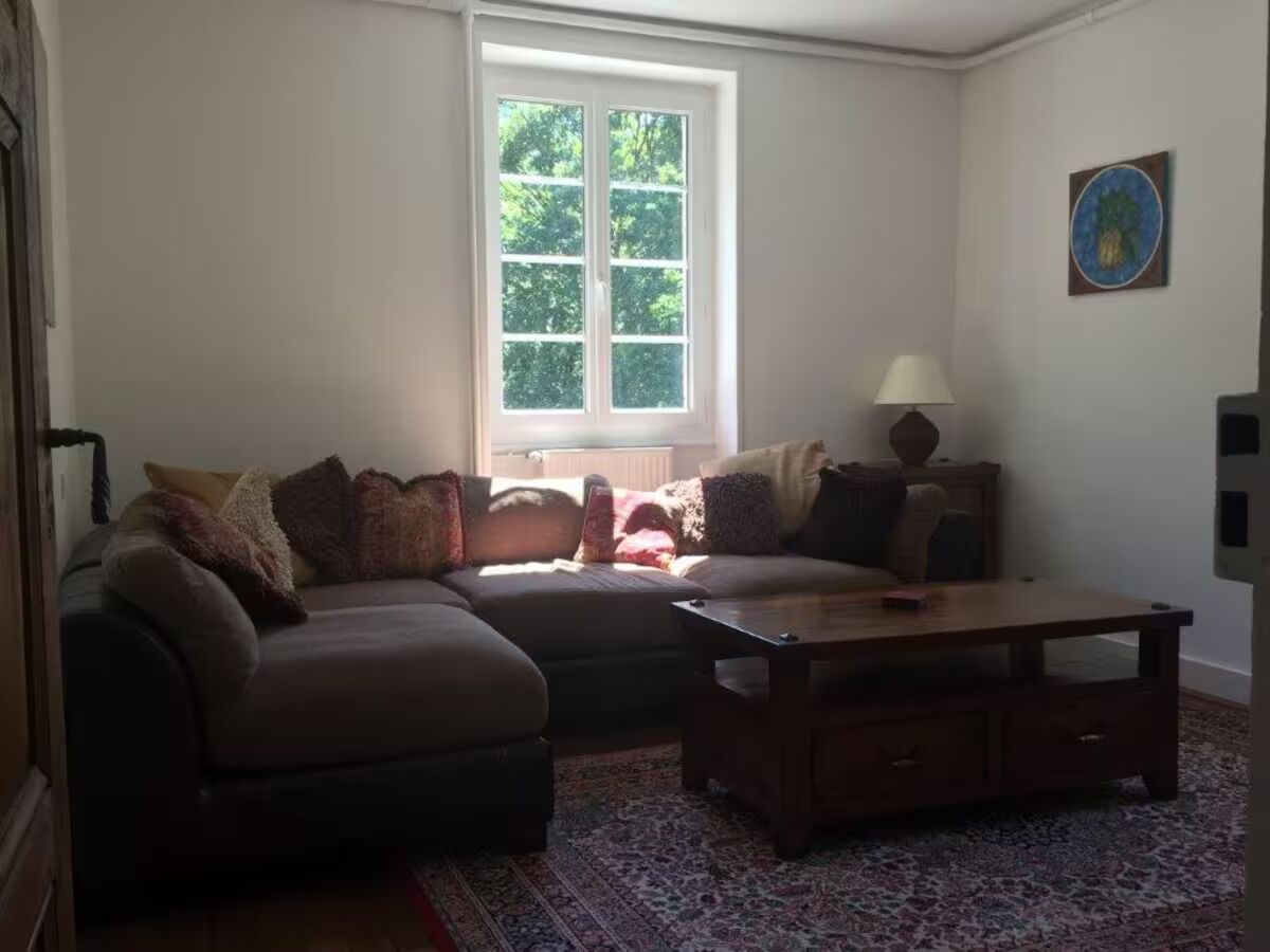 Una sala de estar con sofá, reposapiés, mesa de centro y una ventana con persianas.