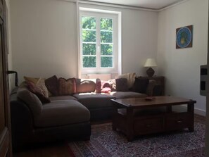 Ein Wohnzimmer mit Sofa, Hocker, Couchtisch und einem Fenster mit Jalousien.