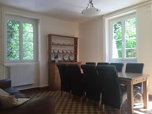 A dining area with a table and chairs, a bookshelf, and a window with a view of greenery. - Country House with Pool (Accommodates up to 20 People) - Dordogne Valley (Servières-le-Château)