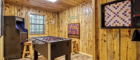 Una habitación con paredes de madera, una mesa de fútbol de mesa, un dardo y una máquina tragamonedas.