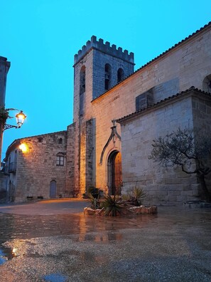 Un edificio histórico de piedra con una torre, un arco de entrada y un patio con un farol.