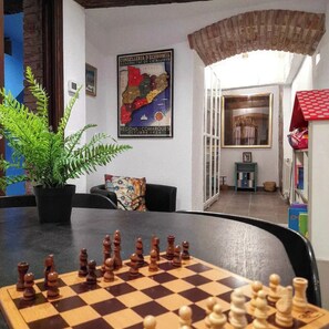 A chessboard set on a table in a room with a map on the wall, a plant, and a small table with a picture frame. - Cal Passió, a fully renovated historic home. Next to the Prades Mountains. (Vimbodí i Poblet)
