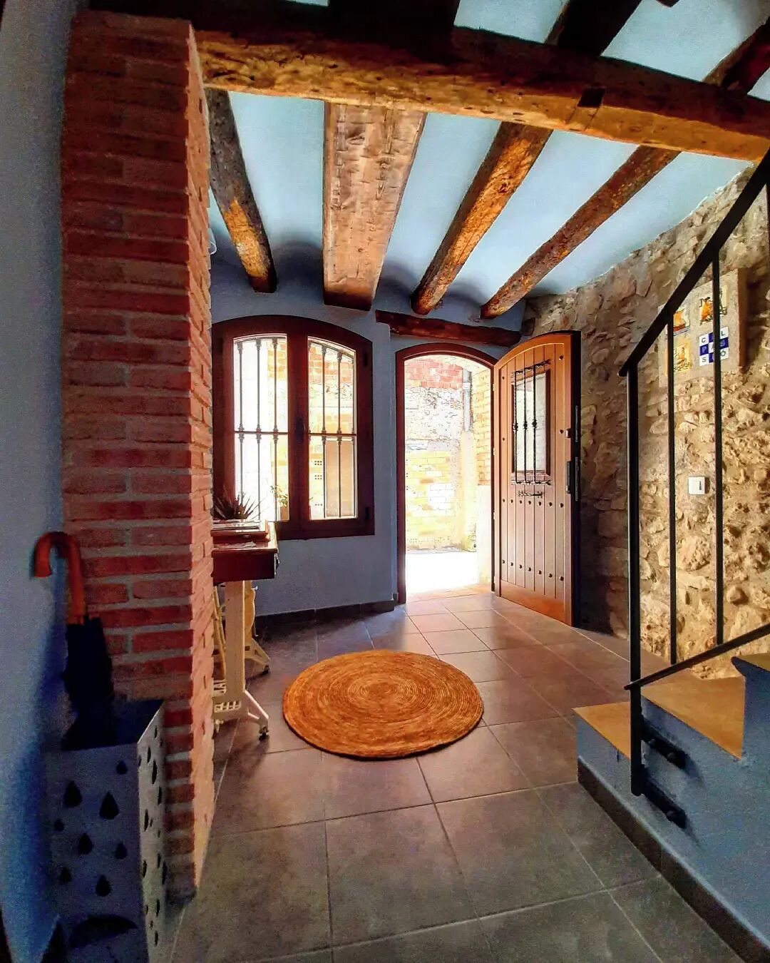 A spacious hallway with a wooden ceiling, a stone wall, and a large window.
