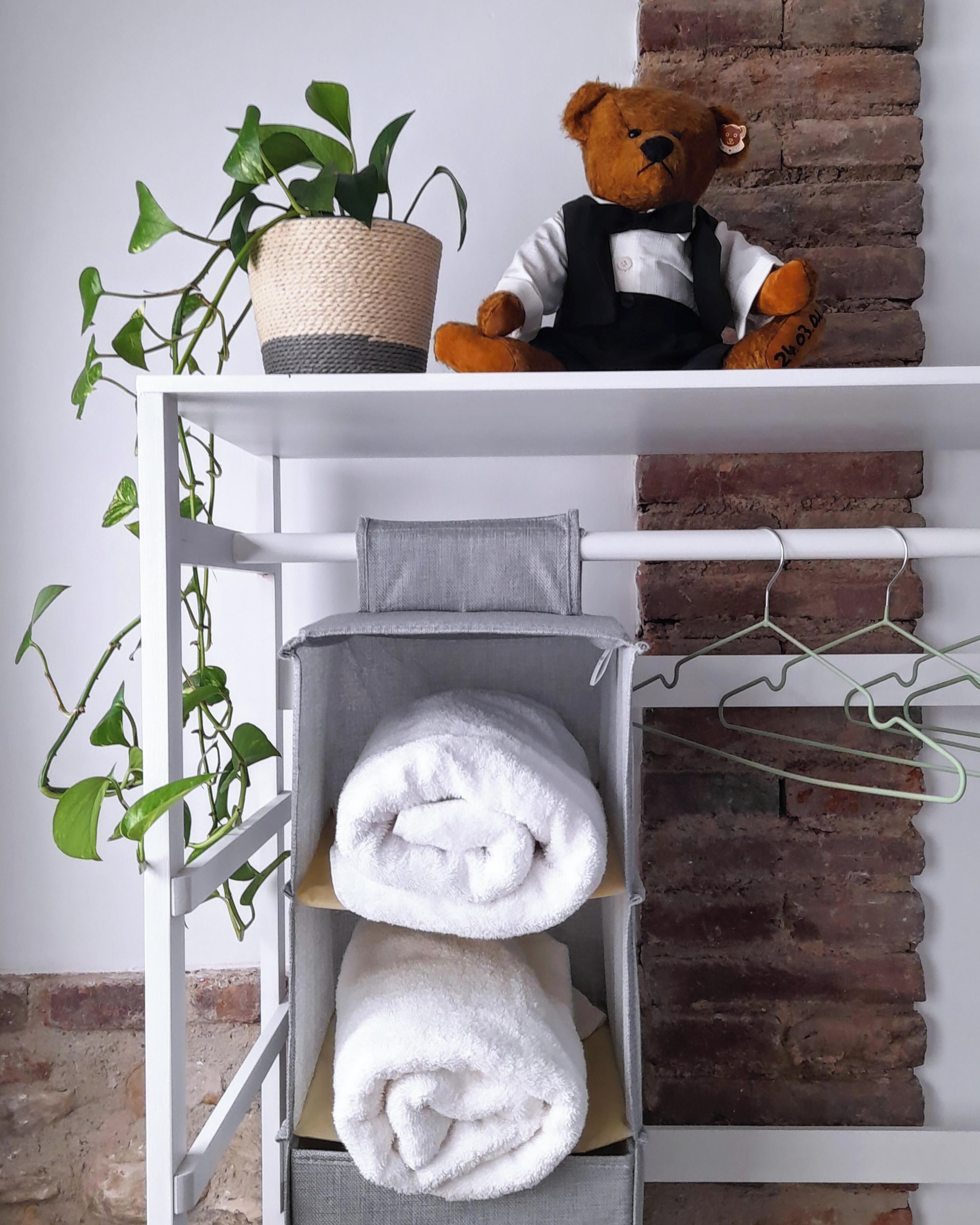 A white metal shelf with a teddy bear, a woven basket, and a potted plant.