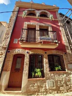 A multi-story building with a red facade, stone walls, and balconies with metal railings. - Cal Passió, a fully renovated historic home. Next to the Prades Mountains. (Vimbodí i Poblet)