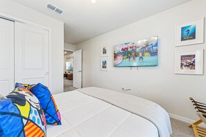 A bedroom with a bed, a chair, and a wall with framed pictures. - Magical 5BR Disney Getaway with Private Pool, Themed Rooms & Resort Amenities (Davenport)