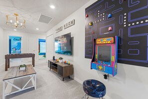 A room with a foosball table, a TV screen displaying 'Title Screens', and a Pac-Man arcade machine. - Magical 5BR Disney Getaway with Private Pool, Themed Rooms & Resort Amenities (Davenport)