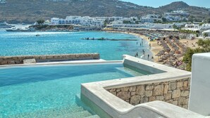 Um resort à beira-mar com piscina cristalina, praia e edifícios brancos.