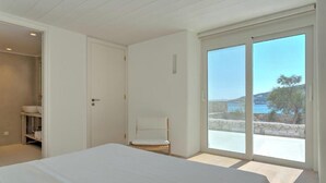 Quarto com cama grande, uma cadeira e vista para o mar através de uma porta deslizante.