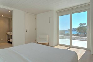 A bedroom with a large bed, a chair, and a view of the sea through a sliding door. - Beachfront Mykon Villa – Your Relaxing Getaway in Platys Gialos (mykonos)