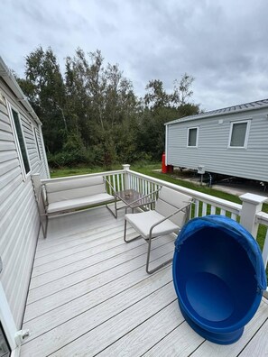 Une terrasse avec un banc et une table, un baril bleu et, au fond, une maison mobile.