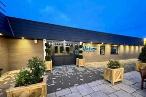 Un edificio con un letrero de 'Welcome', revestimiento de madera y plantas en macetas.