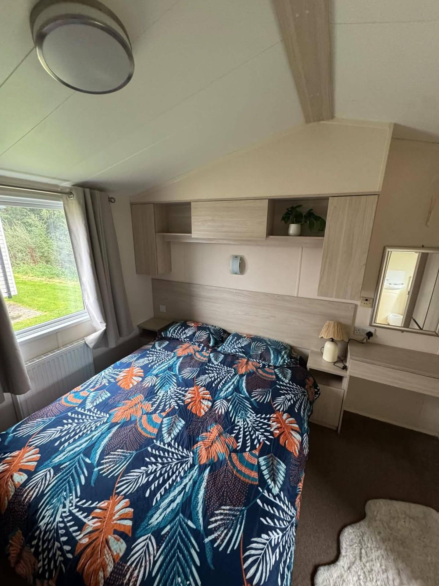 A bedroom with a bed, a desk, a chair, a window, and a plant.