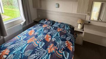 A bedroom with a bed, a desk, a chair, a window, and a plant.