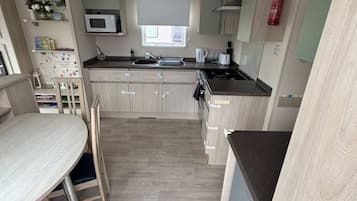 A compact kitchen with a microwave, sink, and stove. There is a dining table with chairs.
