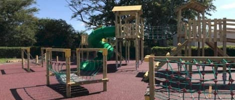 Un parque infantil con un tobogán, estructuras para escalar y una zona delimitada por una red.