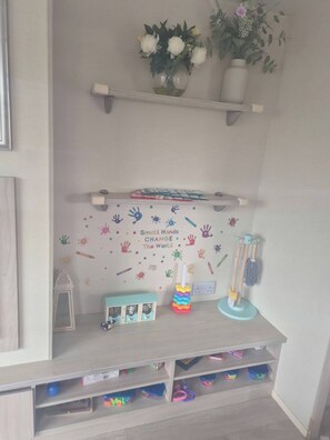 Habitación infantil con un mural de huellas de manos y una cita motivadora, una estantería con juguetes y un pequeño escritorio.