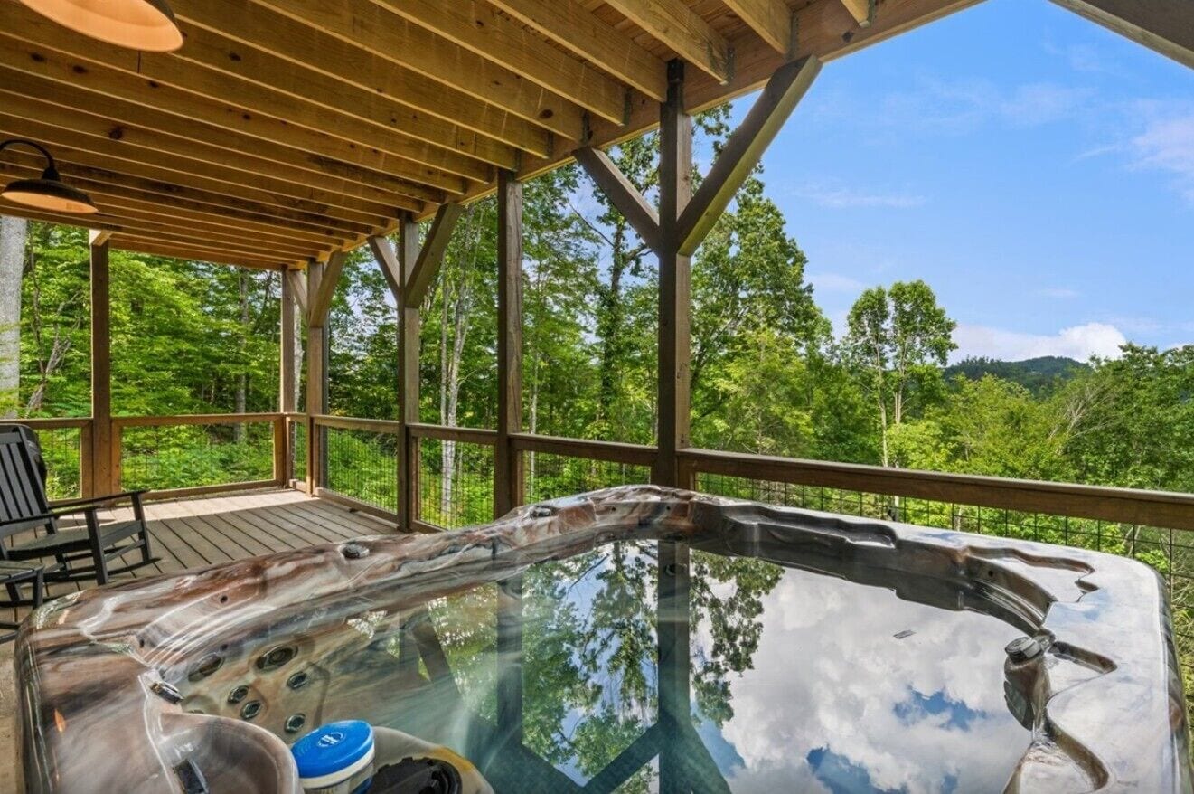 A hot tub with a glass enclosure, wooden deck, and a view of a forested landscape.