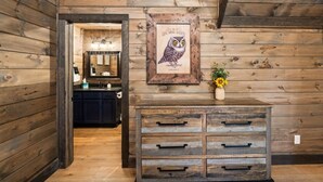 A wooden interior with a framed owl artwork, a dresser with drawers, and a kitchen area in the background. - CoveMtnComf: Pool, MtnViews, HotTub, Wifi, Pets, Theater, Games (Sevierville)