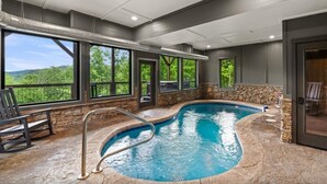 An indoor swimming pool with stone flooring, large windows, and a view of greenery. - CoveMtnComf: Pool, MtnViews, HotTub, Wifi, Pets, Theater, Games (Sevierville)