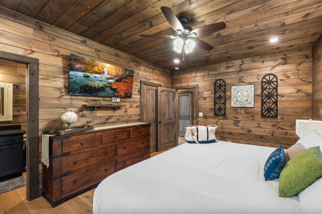 A bedroom with a wooden ceiling, a bed, a dresser, a television, and a ceiling fan.