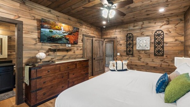 A bedroom with a wooden ceiling, a bed, a dresser, a television, and a ceiling fan. - CoveMtnComf: Pool, MtnViews, HotTub, Wifi, Pets, Theater, Games (Sevierville)