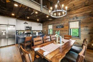 A rustic kitchen with wooden walls, stainless steel appliances, and a dining area with a wooden table and chairs. - CoveMtnComf: Pool, MtnViews, HotTub, Wifi, Pets, Theater, Games (Sevierville)