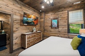 A bedroom with wooden walls, a bed, a dresser, a television, and a window with a view. - CoveMtnComf: Pool, MtnViews, HotTub, Wifi, Pets, Theater, Games (Sevierville)