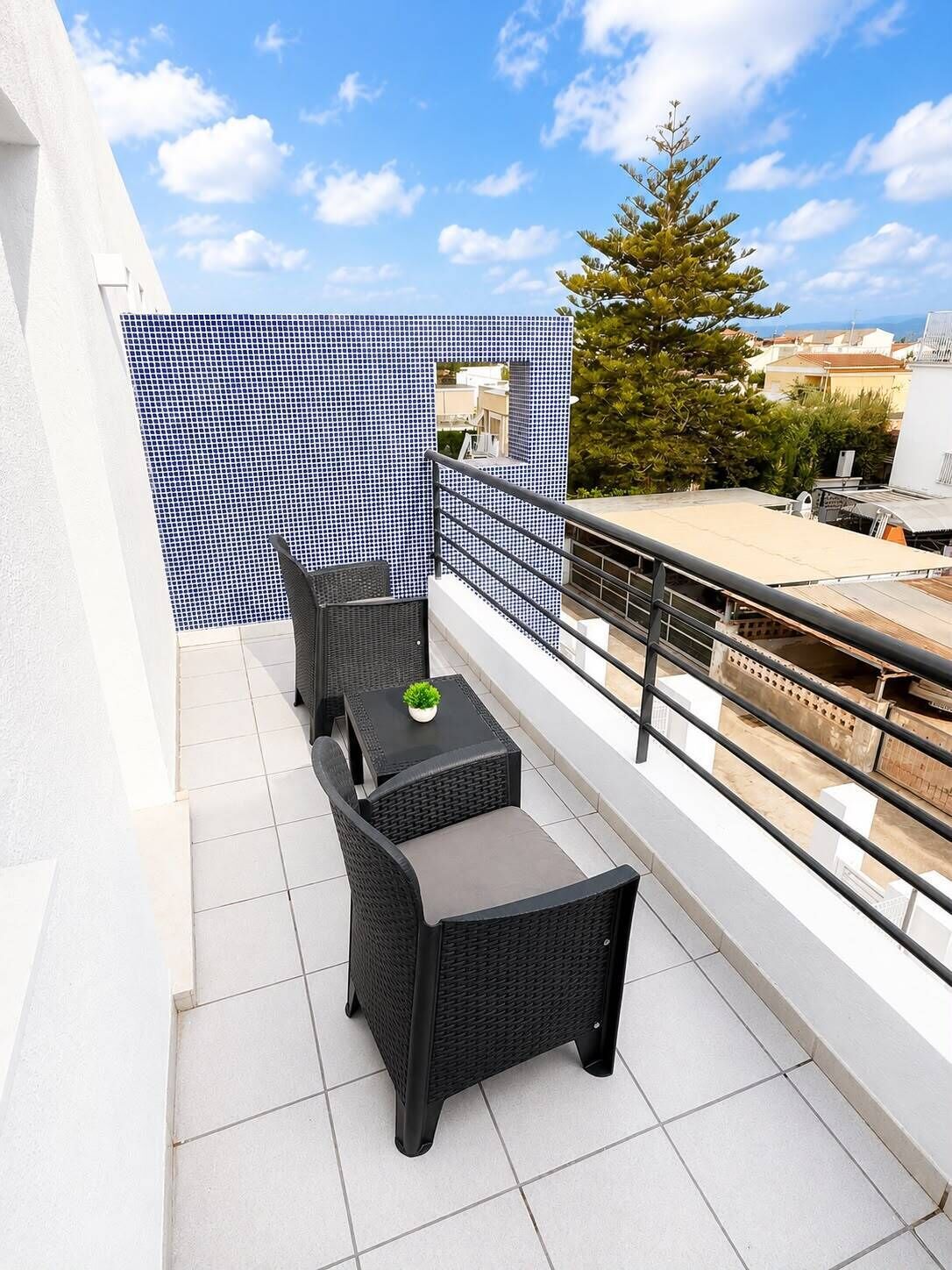 A balcony with a black wicker table and chairs, a small potted plant, and a blue and white patterned wall.