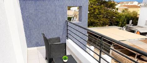 A balcony with a black wicker table and chairs, a small potted plant, and a blue and white patterned wall.