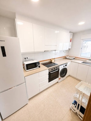 A modern kitchen with white cabinets, a built-in oven, a microwave, and a washing machine. - Townhouse located 50 meters from the beach in a family-friendly and very quiet neighborhood (Almassora)