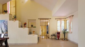 A spacious room with a high ceiling, a dining area with a table and chairs, a small kitchen area, and a large window with curtains. - Villa Terracotta by Redolivenr Art of Living3bhk (Bengaluru)
