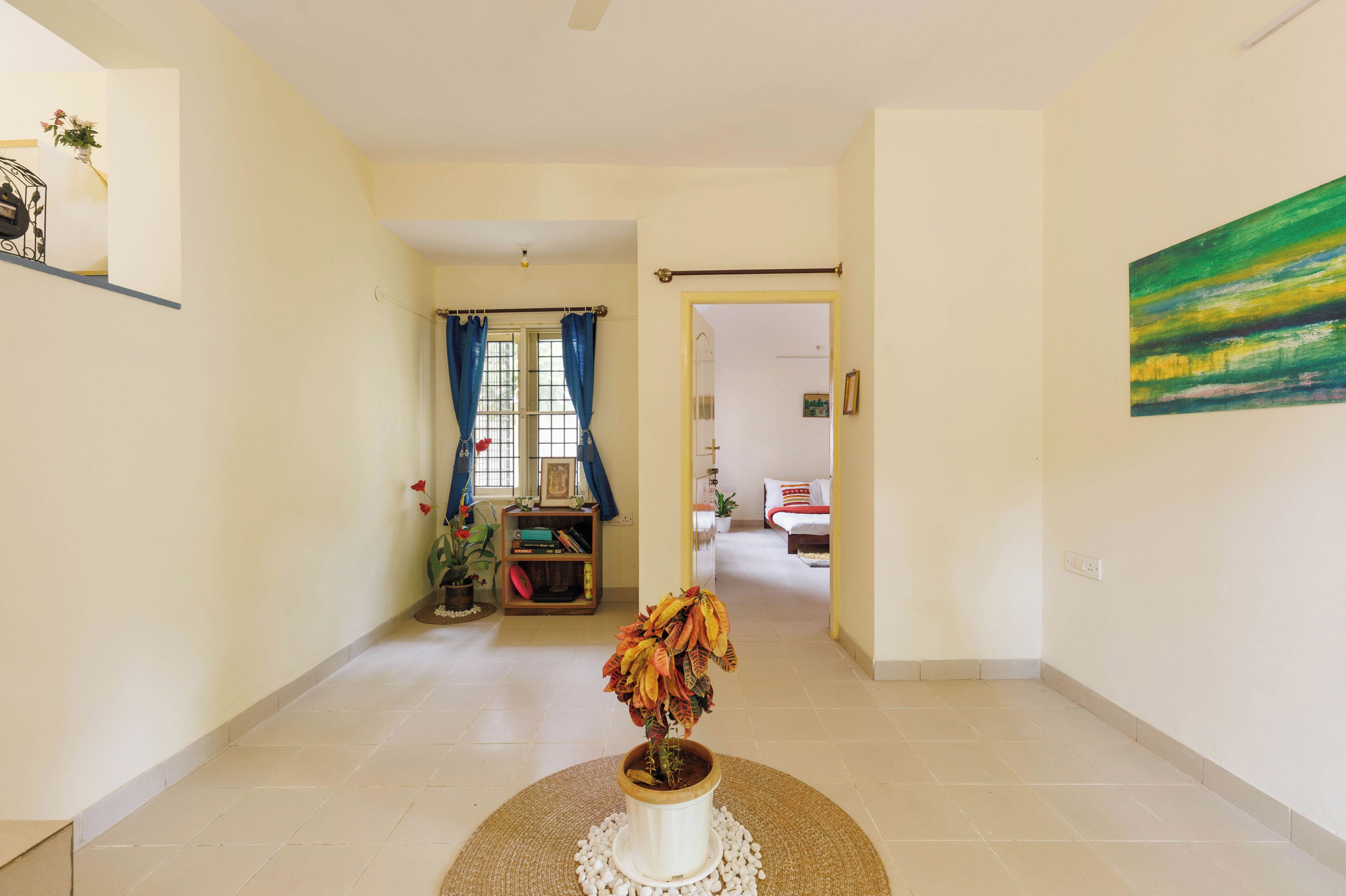 A hallway with a potted plant, a bookshelf, and a bed in the distance.