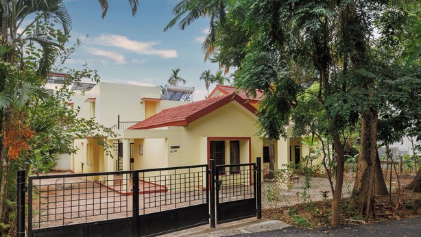 A residential building with a red-tiled roof, a gated entrance, and a paved driveway. - Villa Terracotta by Redolivenr Art of Living3bhk (Bengaluru)