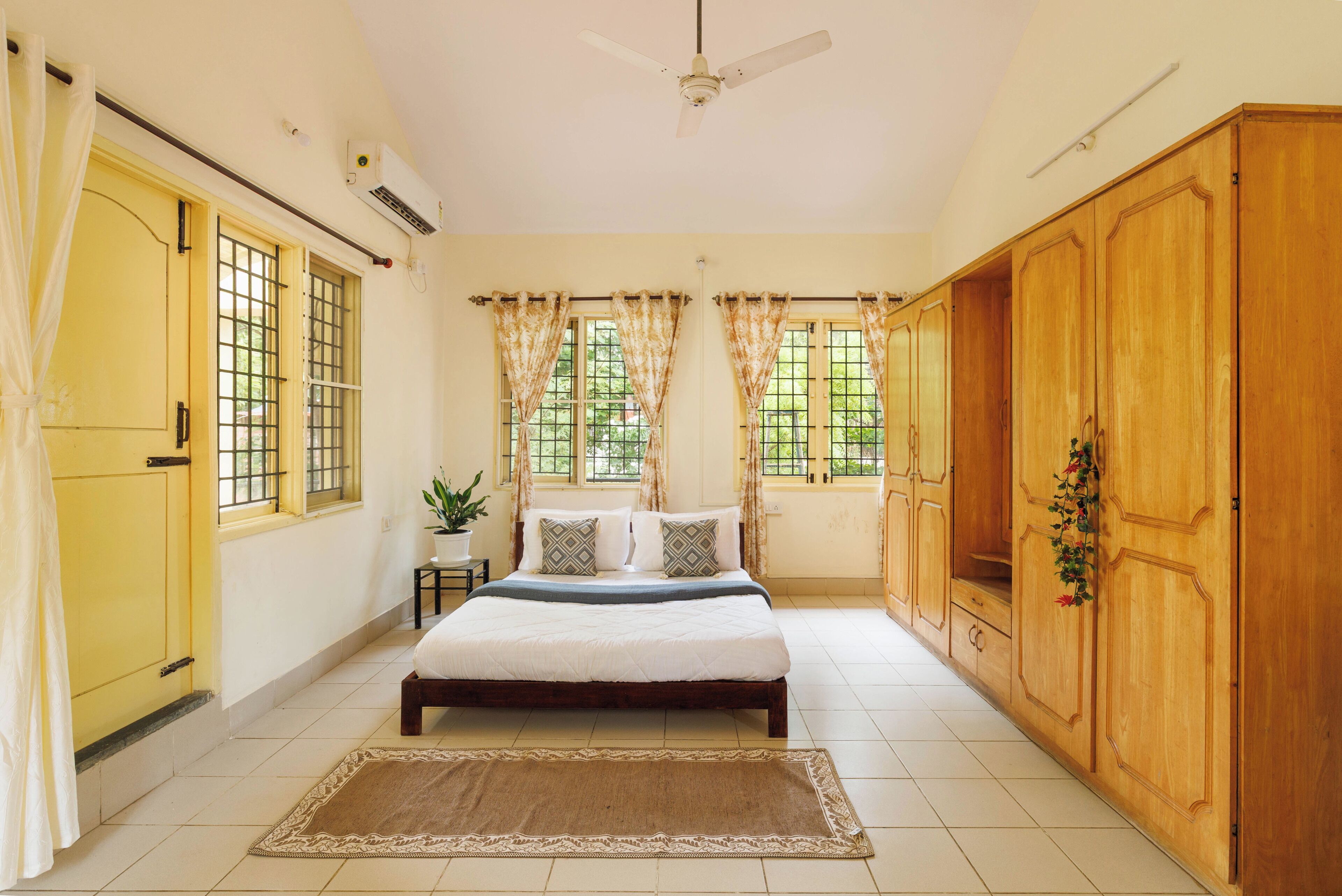 A bedroom with a bed, curtains, a ceiling fan, and a large wardrobe.