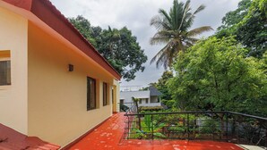 A residential building with a red-tiled roof, a balcony with a metal railing, and lush greenery in the background. - Villa Terracotta by Redolivenr Art of Living3bhk (Bengaluru)