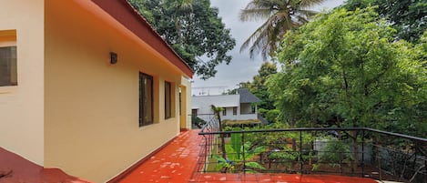 A residential building with a red-tiled roof, a balcony with a metal railing, and lush greenery in the background.