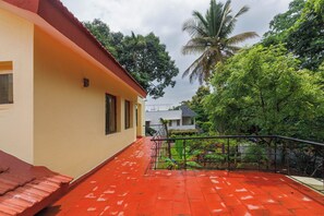 A residential building with a red-tiled roof, a balcony with a metal railing, and lush greenery in the background. - Villa Terracotta by Redolivenr Art of Living3bhk (Bengaluru)