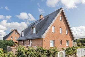 A two-story brick house with a sloped roof, multiple windows, and a visible chimney. - Vrbo Property (Wenningstedt-Braderup (Sylt))