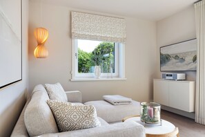 A modern living room with a sofa, a decorative lamp, a window with a view of greenery, and a painting on the wall. - Your modern retreat in Wenningstedt. (Wenningstedt-Braderup (Sylt))